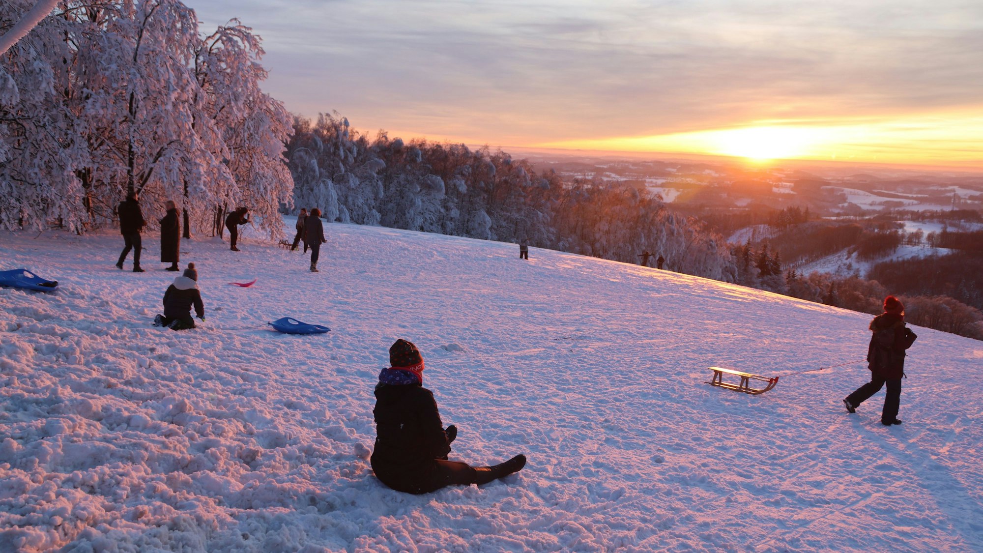 Rodelnde Kinder vor untergehender Sonne.