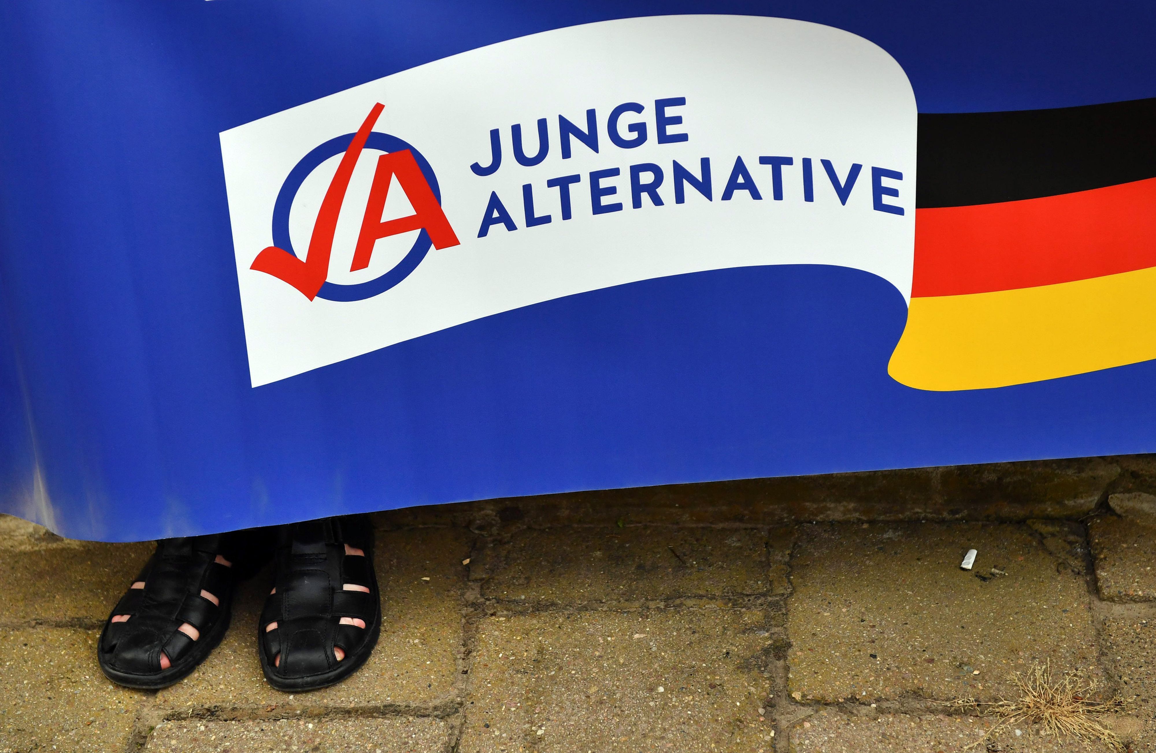 Ein Mann in schwarzen Sandalen hält ein Plakat der AfD-Jugendorganisation Junge Alternative (JA).