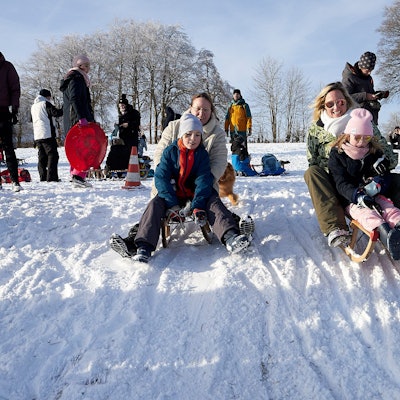 Zahlreiche Besucher rodeln den Abhang hinunter.