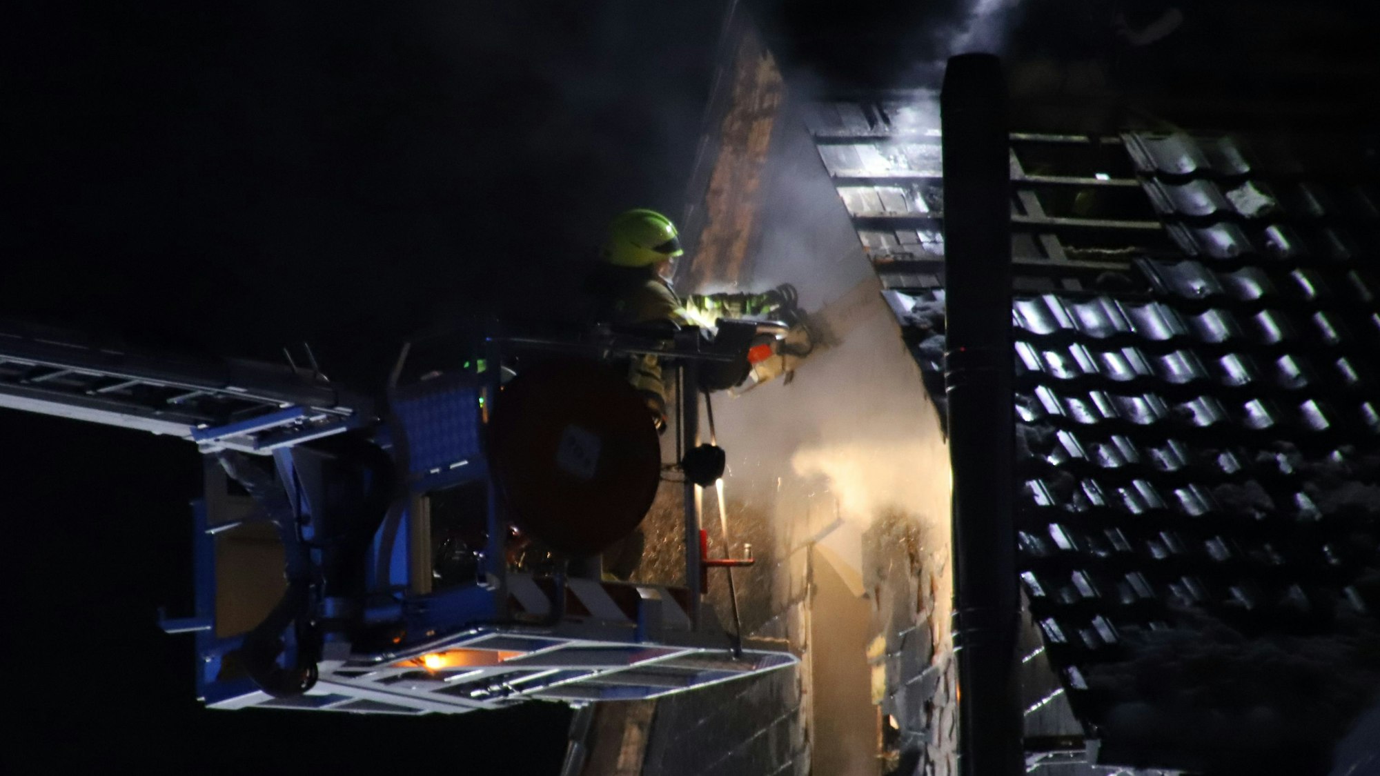 Ein Feuerwehrmann durchschnitt mit einer Motorsäge Verkleidung und Holzbalken. um letzte Glutnester zu finden.