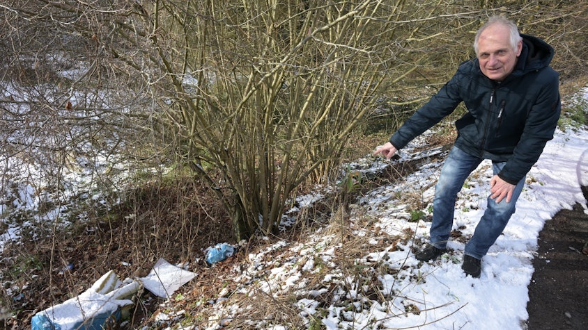 Ein Mann zeigt auf Plastiktüten voller Müll an einer Böschung in Overath-Untereschbach.