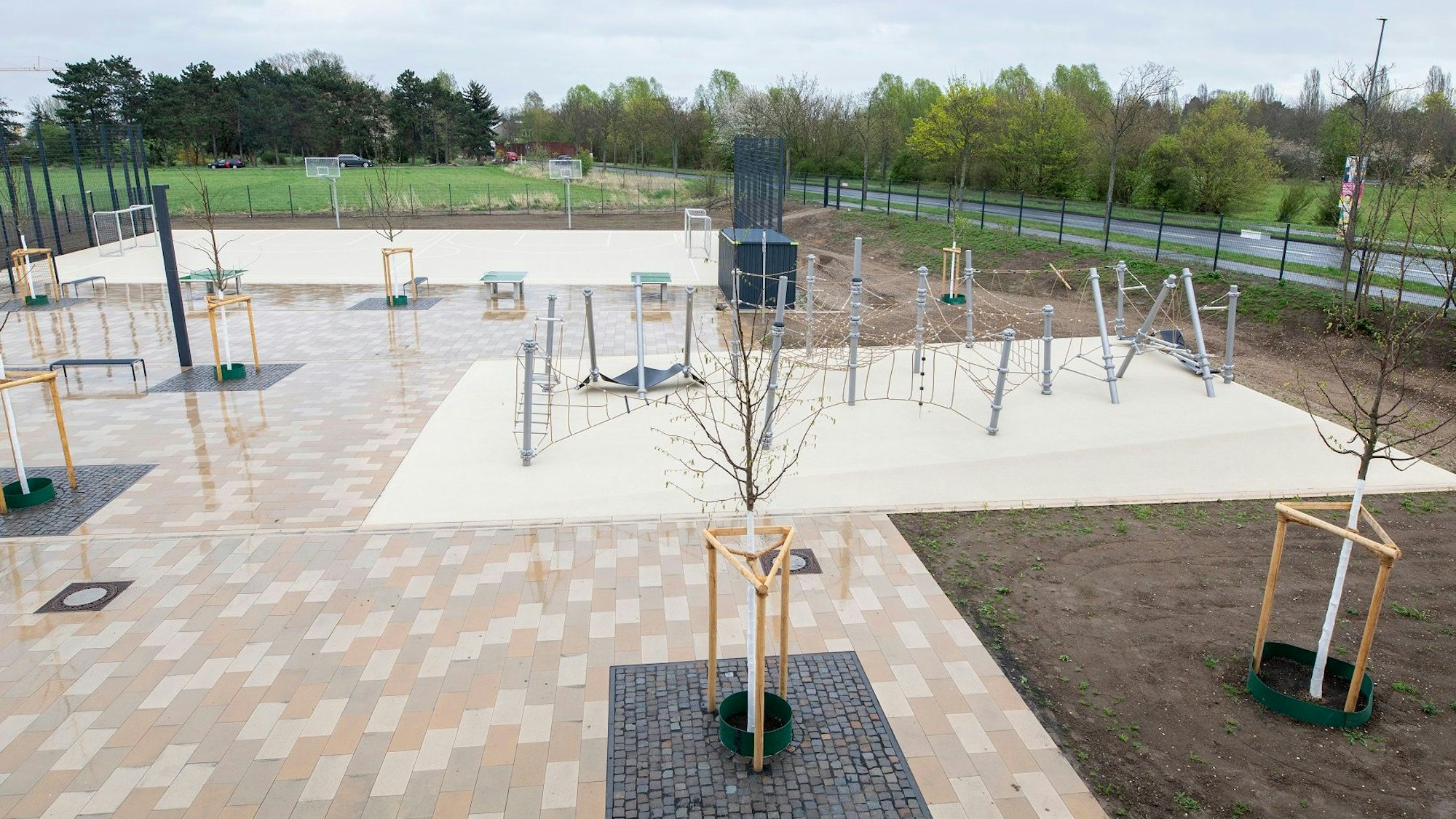 Ein frisch angelegter Schulhof mit Klettergerüst und frisch gepflanzten Bäumen ist zu sehen.