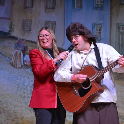 Robert Becker spielt auf der Bühne Gitarre und singt dazu, Birte Karstens hält für ihn das Mikrofon.