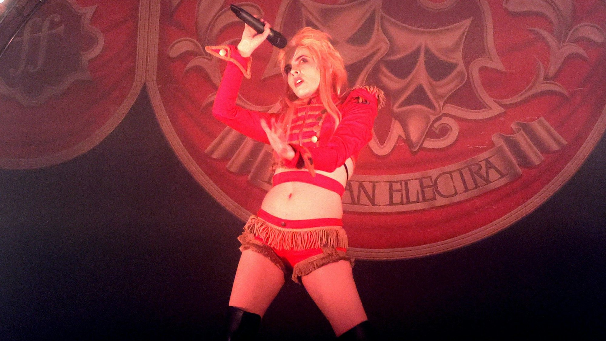 Dorian Electra trägt eine Fantasieuniform mit Troddeln und knappen Shorts. Die blonden Haare erinnern an David Bowies Frisur im Film „Labyrinth“.