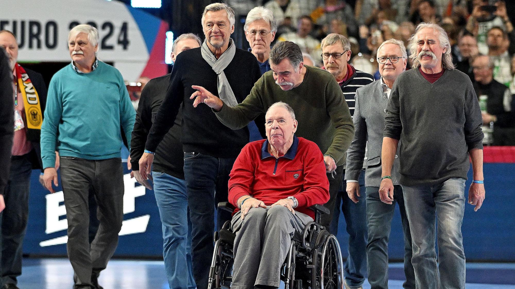 Mit Heiner Brand und seinen ehemaligen Teamkollegen ist Joachim Deckarm (im Rollstuhl) in die Lanxess Arena nach Köln gekommen. Die Gruppe steht auf dem Handballfeld.