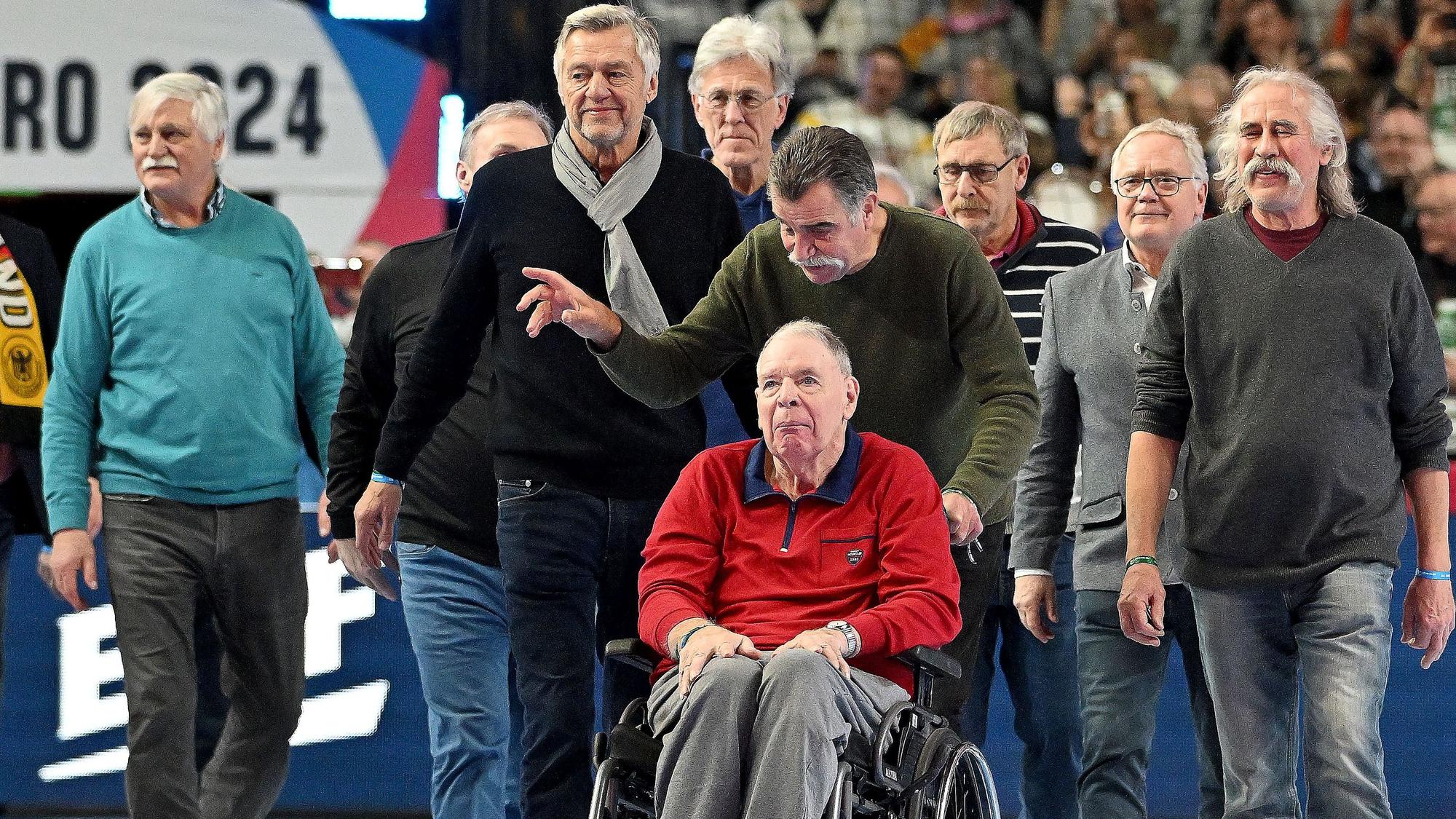 In seinem Rollstuhl, geschoben von Heiner Brand, führt Jo Deckarm die 78er Weltmeister in der Lanxess-Arena an.