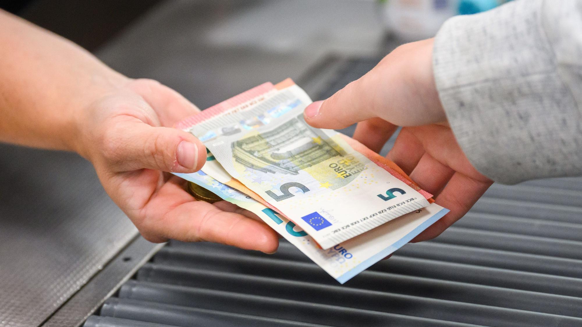 An der Kasse eines Supermarkts werden Scheine von einer Hand in eine andere gereicht.