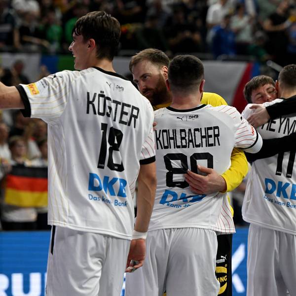Die deutsche Handballmannschaft umarmt sich und jubelt vor einem unscharfen Publikum im Hintergrund.