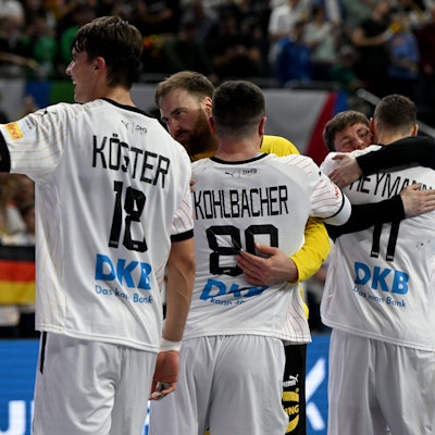 Die deutsche Handballmannschaft umarmt sich und jubelt vor einem unscharfen Publikum im Hintergrund.