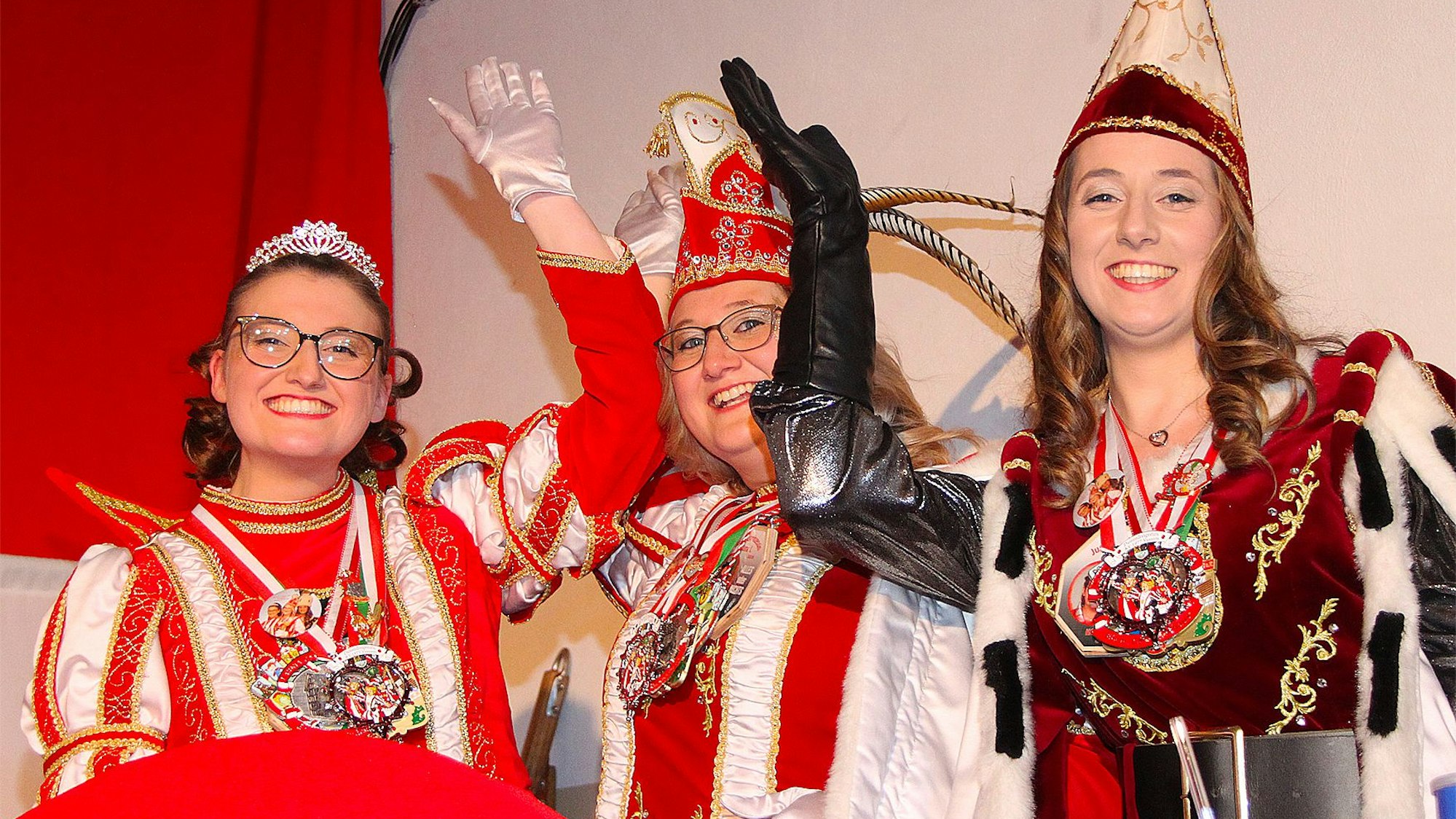 Die drei Frauen, die das Dreigestirn bilden, lachen fröhlich in die Kamera. Sie tragen jeweils mehrere Karnevalsorden.