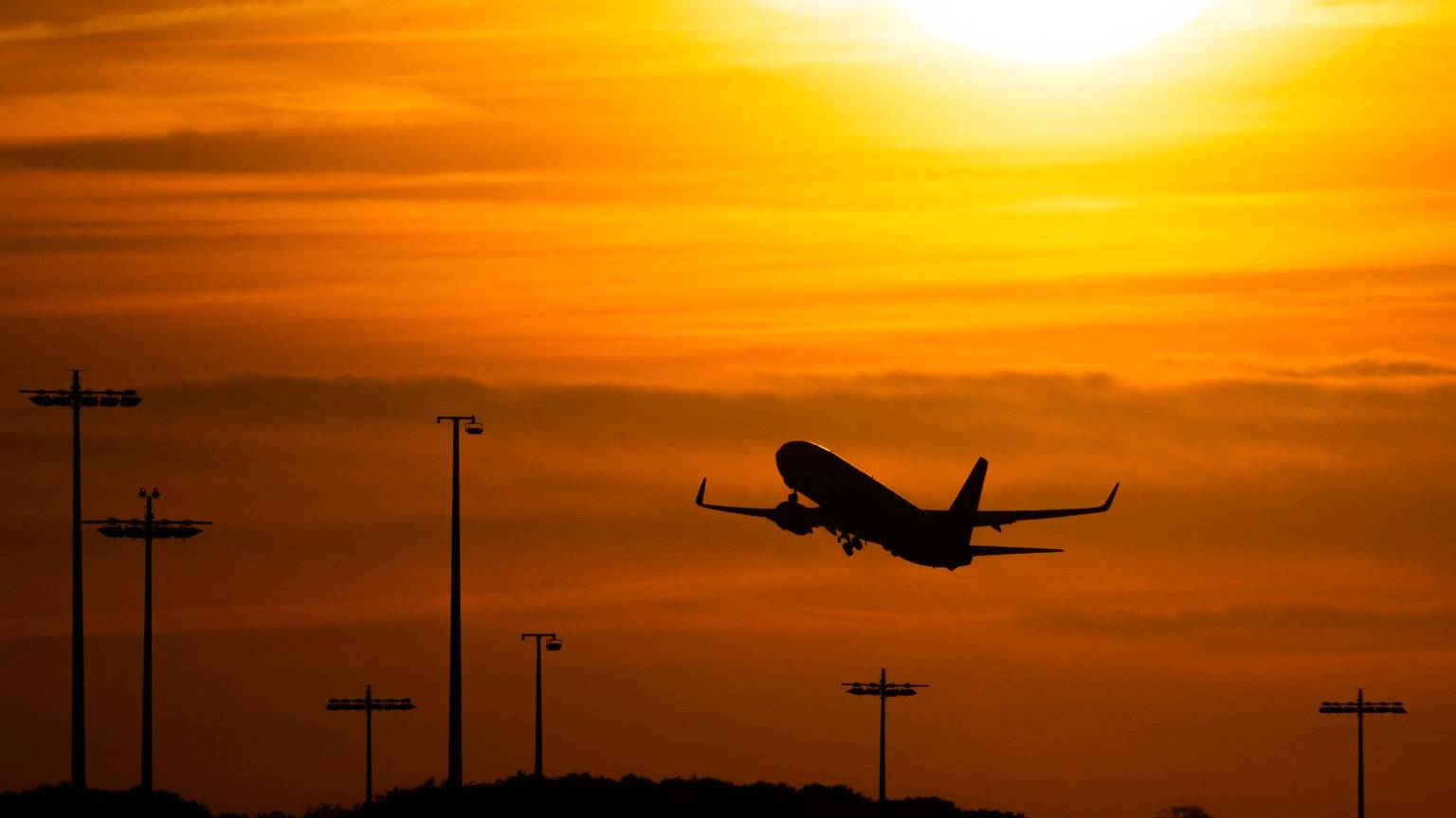 Hamburg: Ein Passagierflugzeug befindet sich am Flughafen von Hamburg im Steigflug vor der untergehenden Sonne.