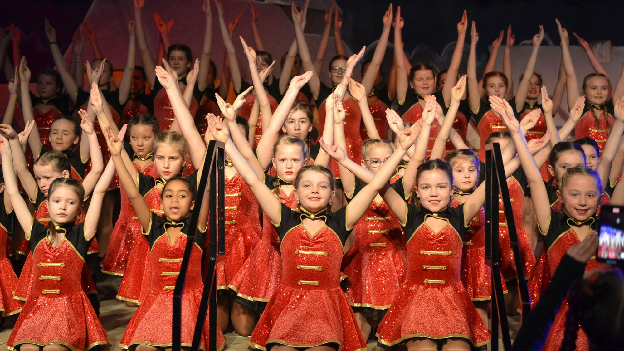 75 junge Tänzerinnen in roten Kleidern strecken die Arme aus.