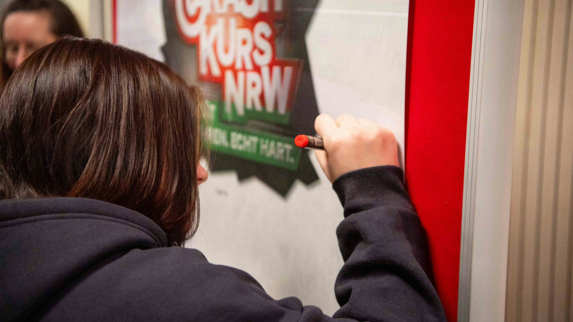 Das Bild zeigt eine Berufsschülerin, wie sie an einer Stellwand unterschreibt.