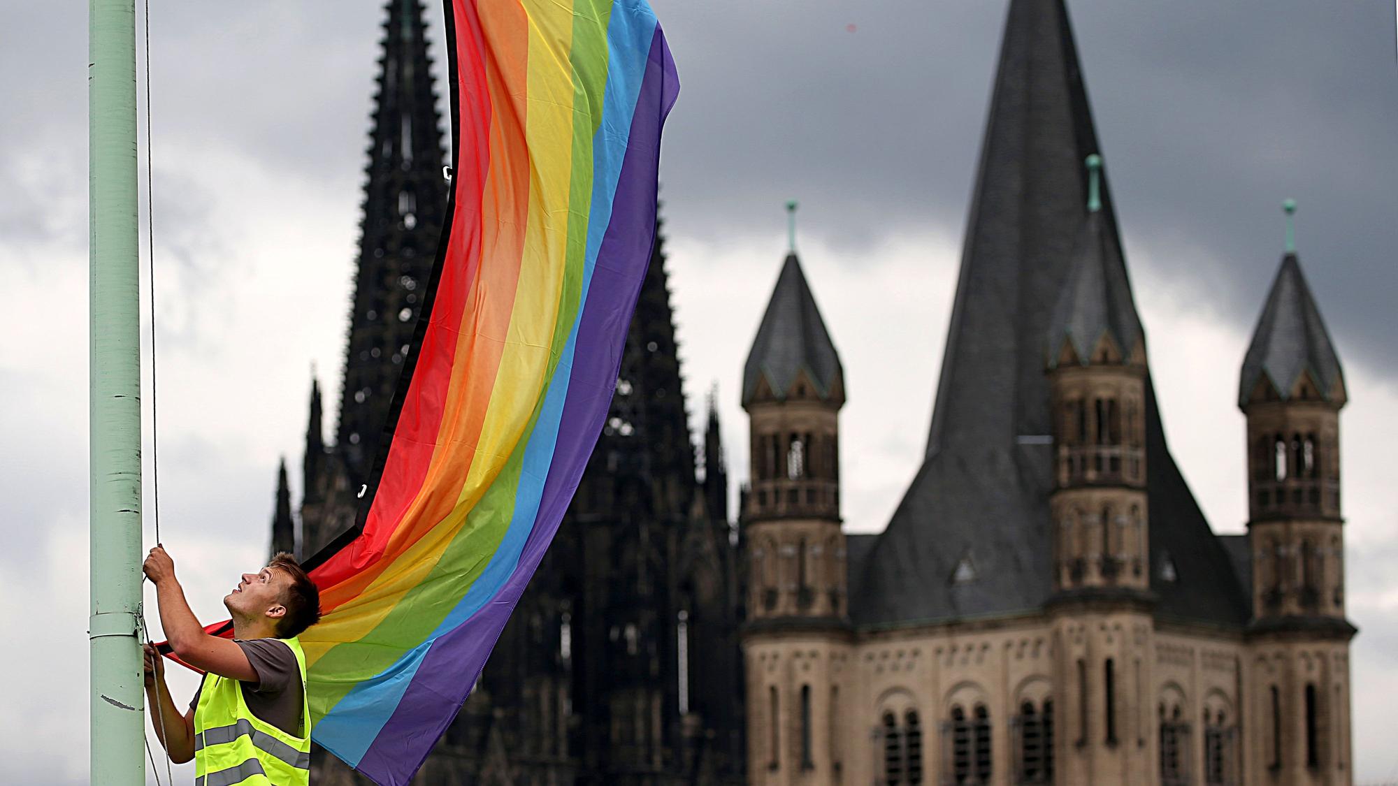 Ein Arbeiter hängt nach der Entscheidung im Bundestag über die «Ehe für alle» vor der Kulisse des Kölner Doms und der Kirche Groß St. Martin (r.) eine Regenbogenfahne auf. Mehr als 200 Theologieprofessoren haben in einer gemeinsamen Stellungnahme gegen das Segnungsverbot des Vatikans für homosexuelle Paare protestiert.
