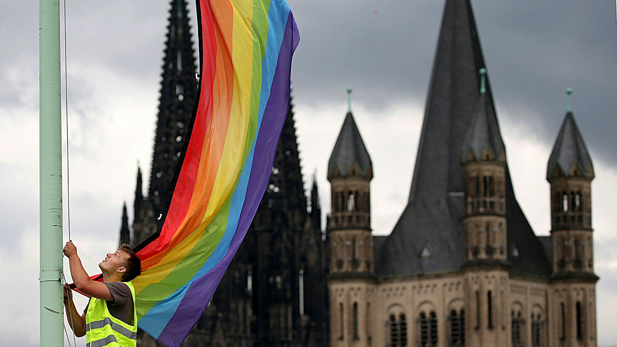 Ein Arbeiter hängt nach der Entscheidung im Bundestag über die «Ehe für alle» vor der Kulisse des Kölner Doms und der Kirche Groß St. Martin (r.) eine Regenbogenfahne auf. Mehr als 200 Theologieprofessoren haben in einer gemeinsamen Stellungnahme gegen das Segnungsverbot des Vatikans für homosexuelle Paare protestiert.