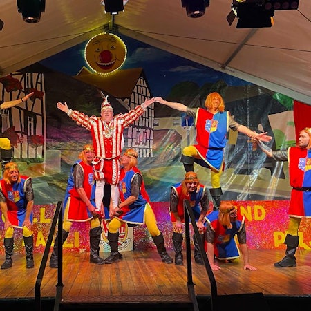 Tänzer des Männerballetts haben Prinz Kalli in eine artistische Nummer integriert. Zwei Mitglieder tragen ihn auf ihren Händen. Er streckt die Arme nach oben.