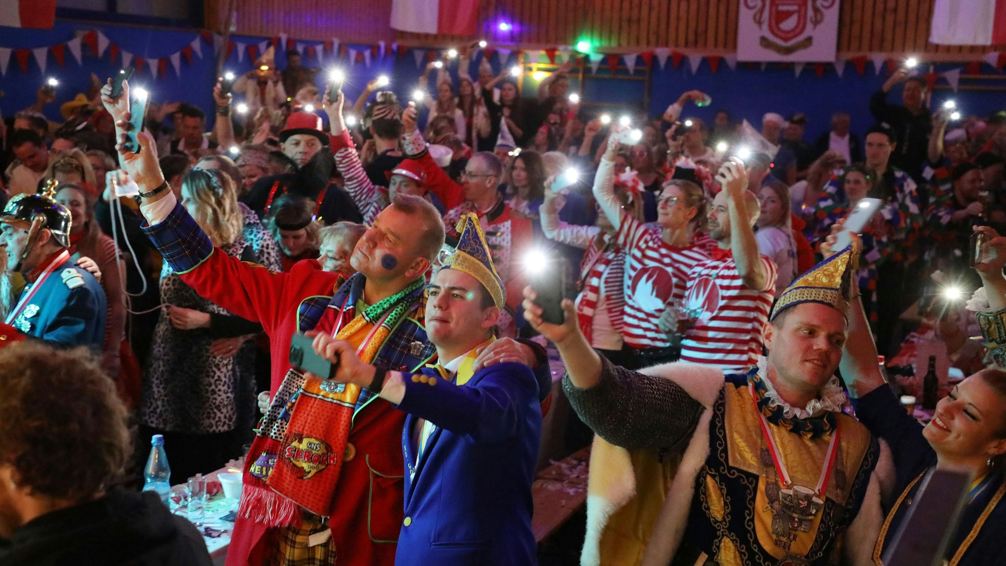 Kostümierte Menschen halten in einer abgedunkelten Halle Lichter in die Höhe.