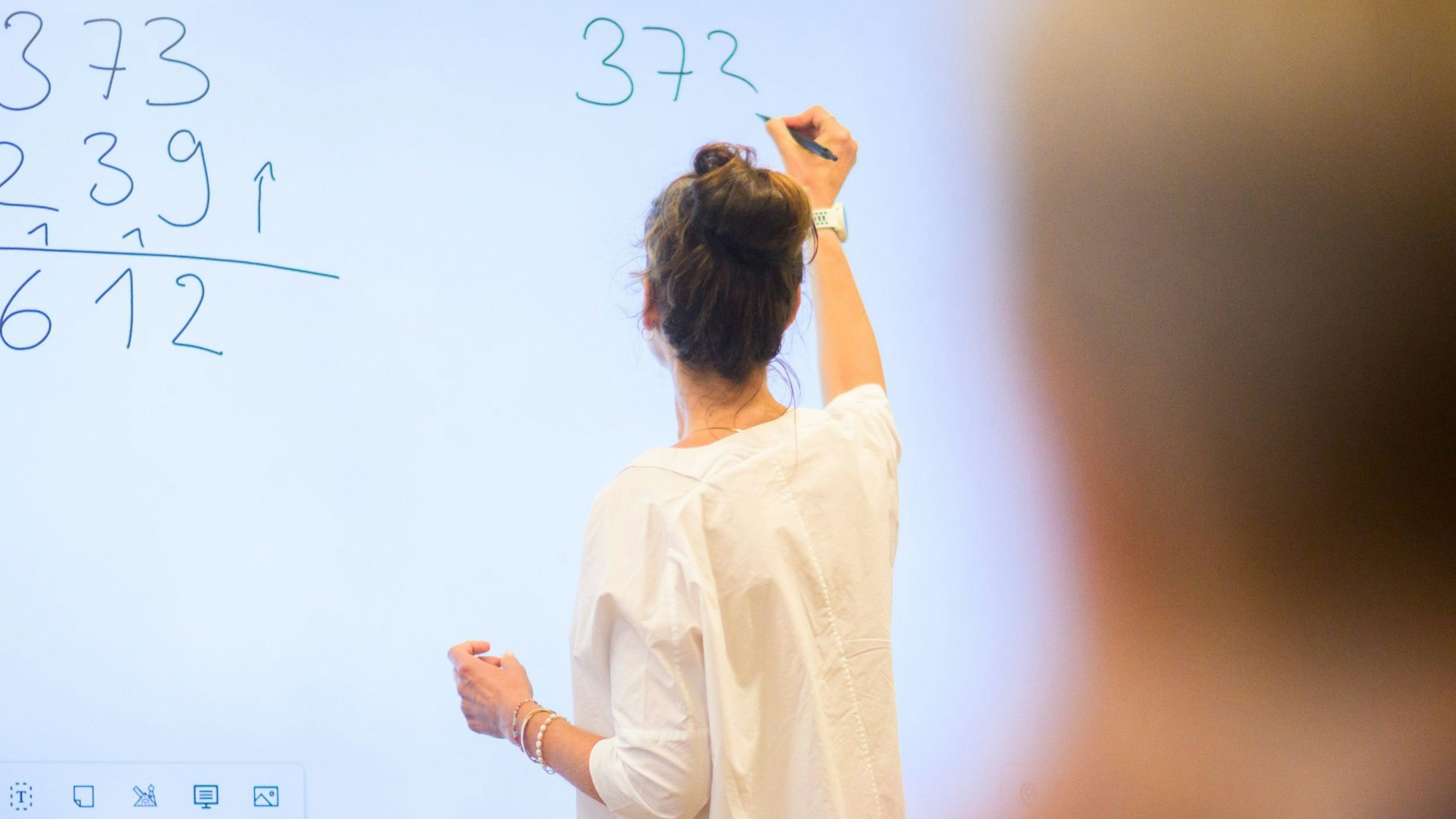 Eine Lehrerin rechnet an einer digitalen Tafel.