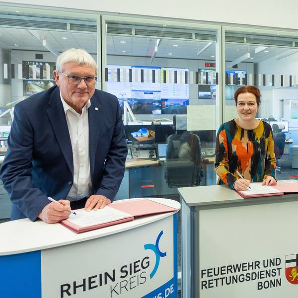 Landrat Sebastian Schuster, Bonns Oberbürgermeisterin Katja Dörner und Prof. Wolfgang Holzgreve, Ärztlicher Direktor des Universitätsklinikums Bonn (UKB), stehen in der Bonner Feuerwache 1 an Pulten und unterschreiben eine gemeinsame Vereinbarung.