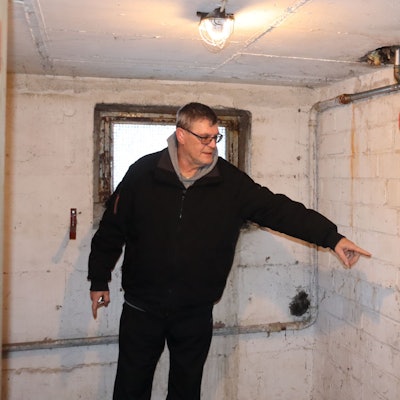 Ein Mann zeigt auf eine braune Spur an einer Kellerwand.