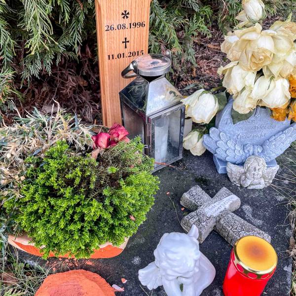 Das Bild zeigt den Gedenkort einer jungen Frau, die in Euskirchen bei einem Verkehrsunfall ums Leben gekommen ist. Vor dem Kreuz stehen Kerze und Blumen.