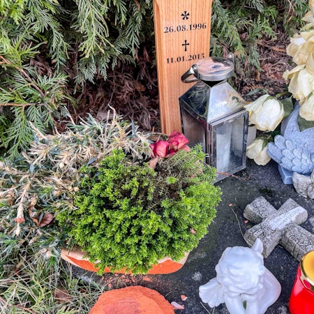 Das Bild zeigt den Gedenkort einer jungen Frau, die in Euskirchen bei einem Verkehrsunfall ums Leben gekommen ist. Vor dem Kreuz stehen Kerze und Blumen.