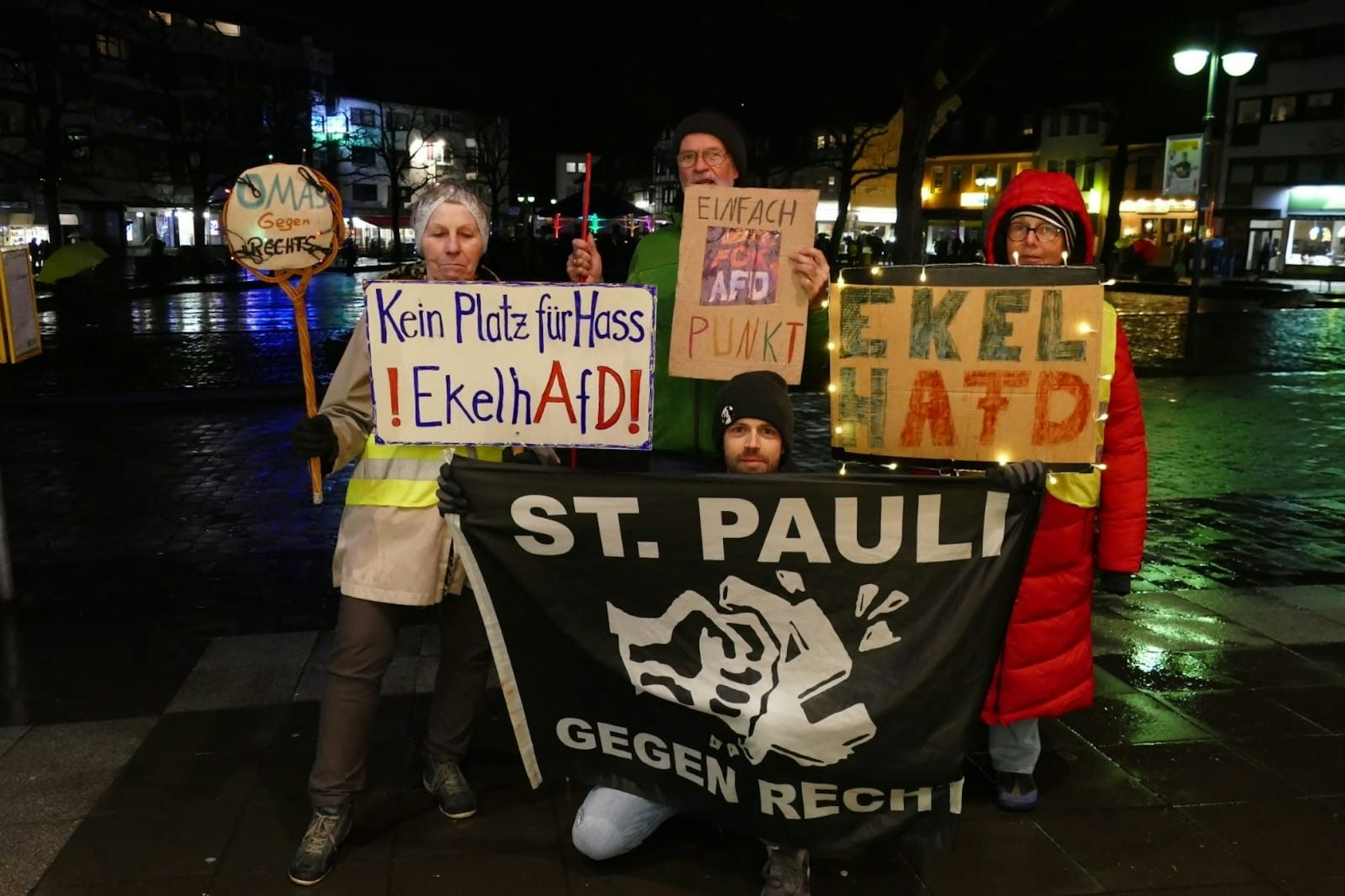 Zwei Frauen und zwei Männer halten Plakate und Fahnen in die Höhe.