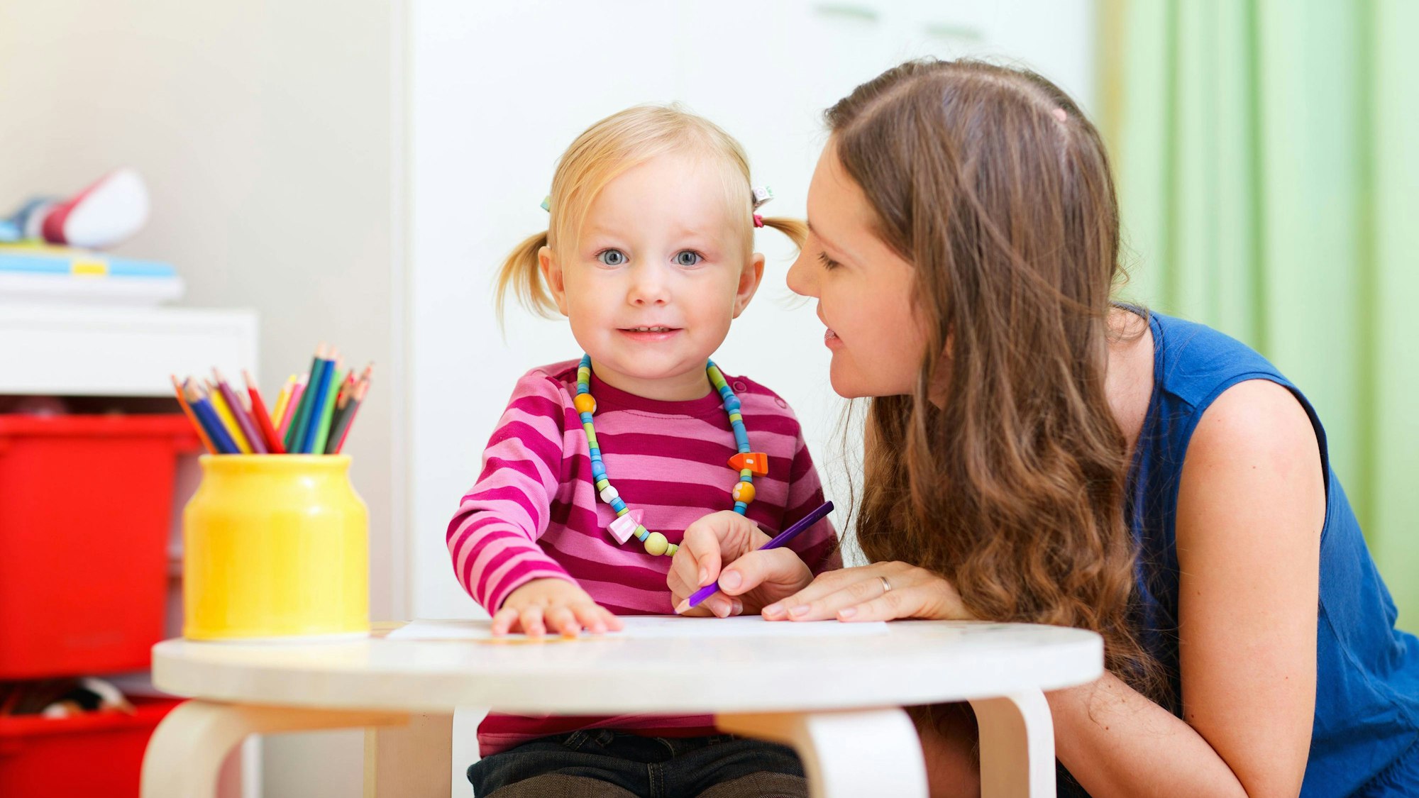 Für viele Familien ist es eine Herausforderung, einen Babysitter zu finden. Im Bild sitzt ein kleines Mädchen in einem Hochstuhl, eine junge Frau sitzt daneben.