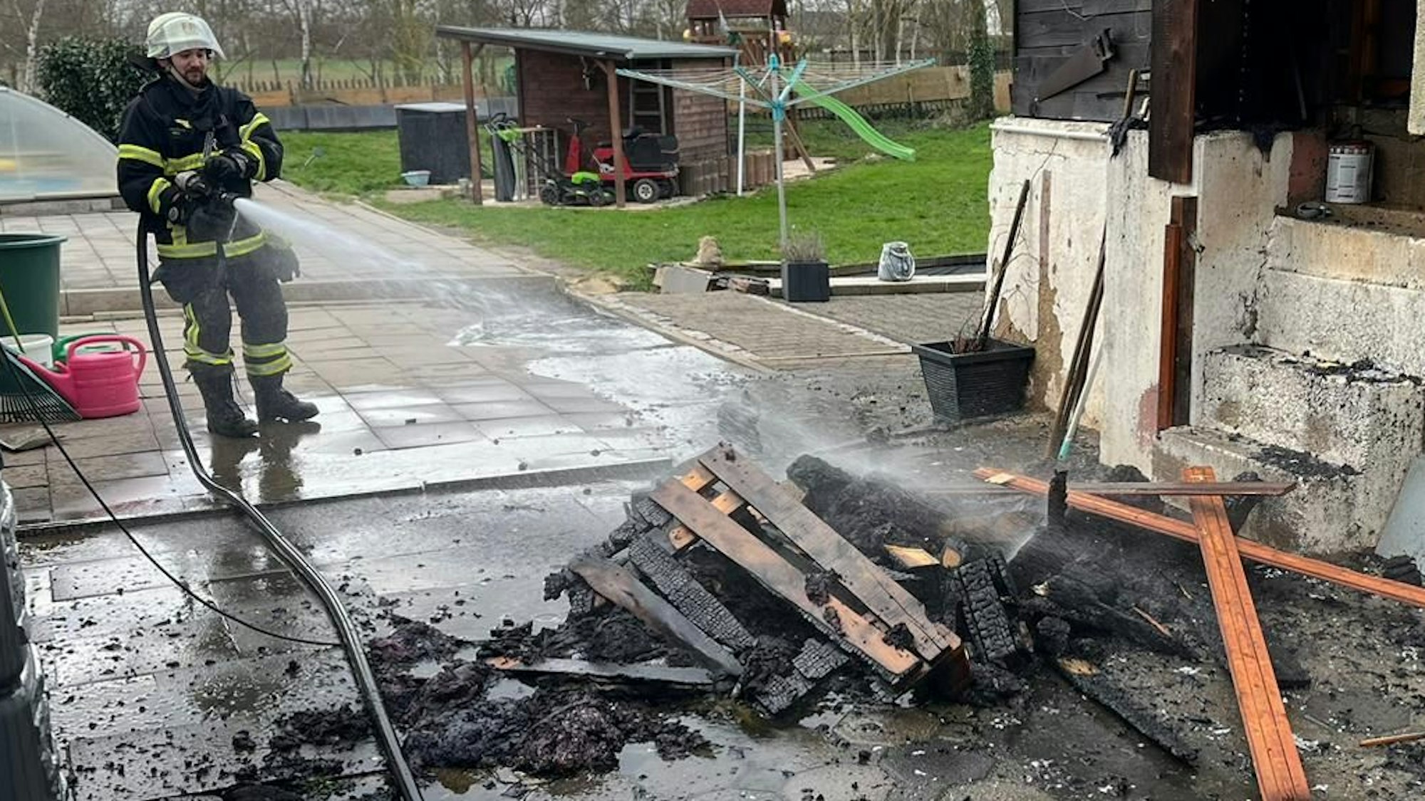 Das Bild zeigt Feuerwehrleute beim Löschen von Holzmöbeln.