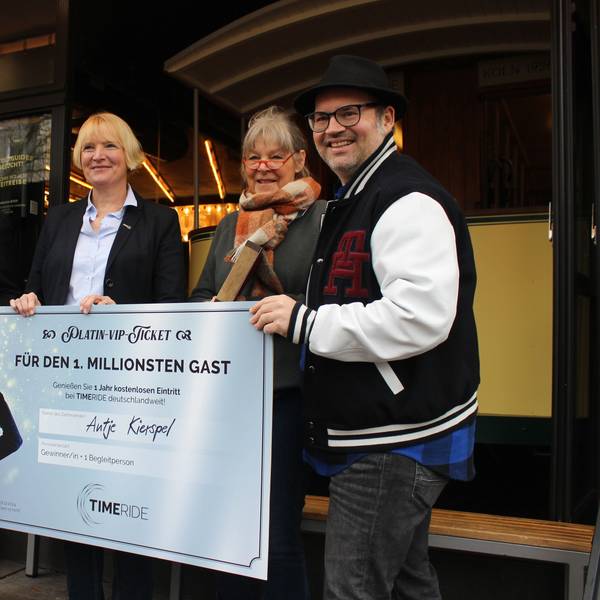 Zwei Männer und drei Frauen vor einem Check mit der Aufschrift „für den 1. Millionsten Gast“