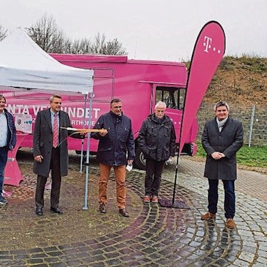 Der damalige Niederkasseler Bürgermeister Stephan Vehreschild und Vertreter von Telekom, Politik und Stadtverwaltung stehen vor einem magentafarbenen Infomobil der Telekom.