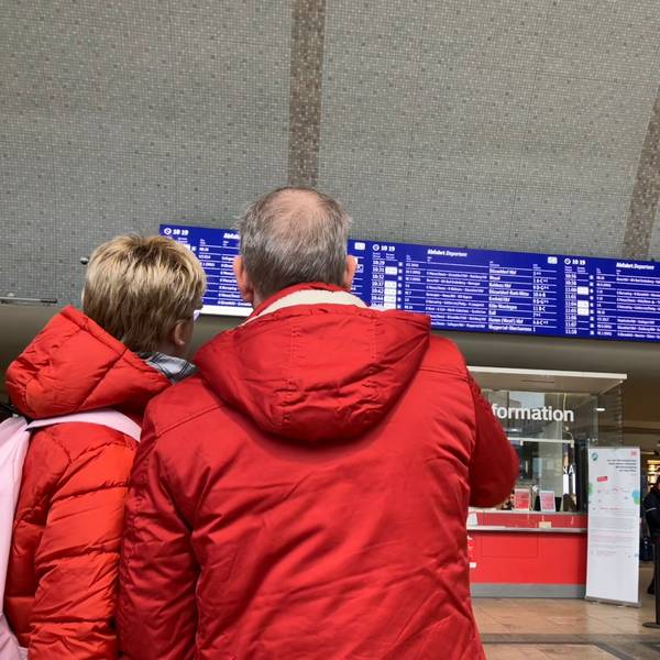 Ein Paar in Winterjacken sucht auf der Anzeigetafel im Kölner Hauptbahnhof nach einem Zug.