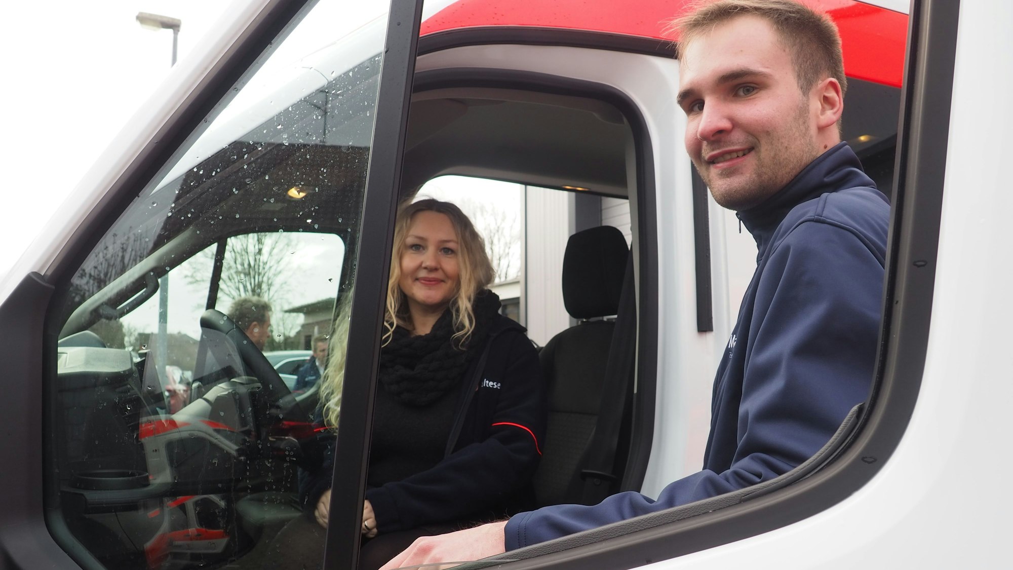Eine Frau sitzt am Steuer eines Autos, ein Mann steht an der Tür.