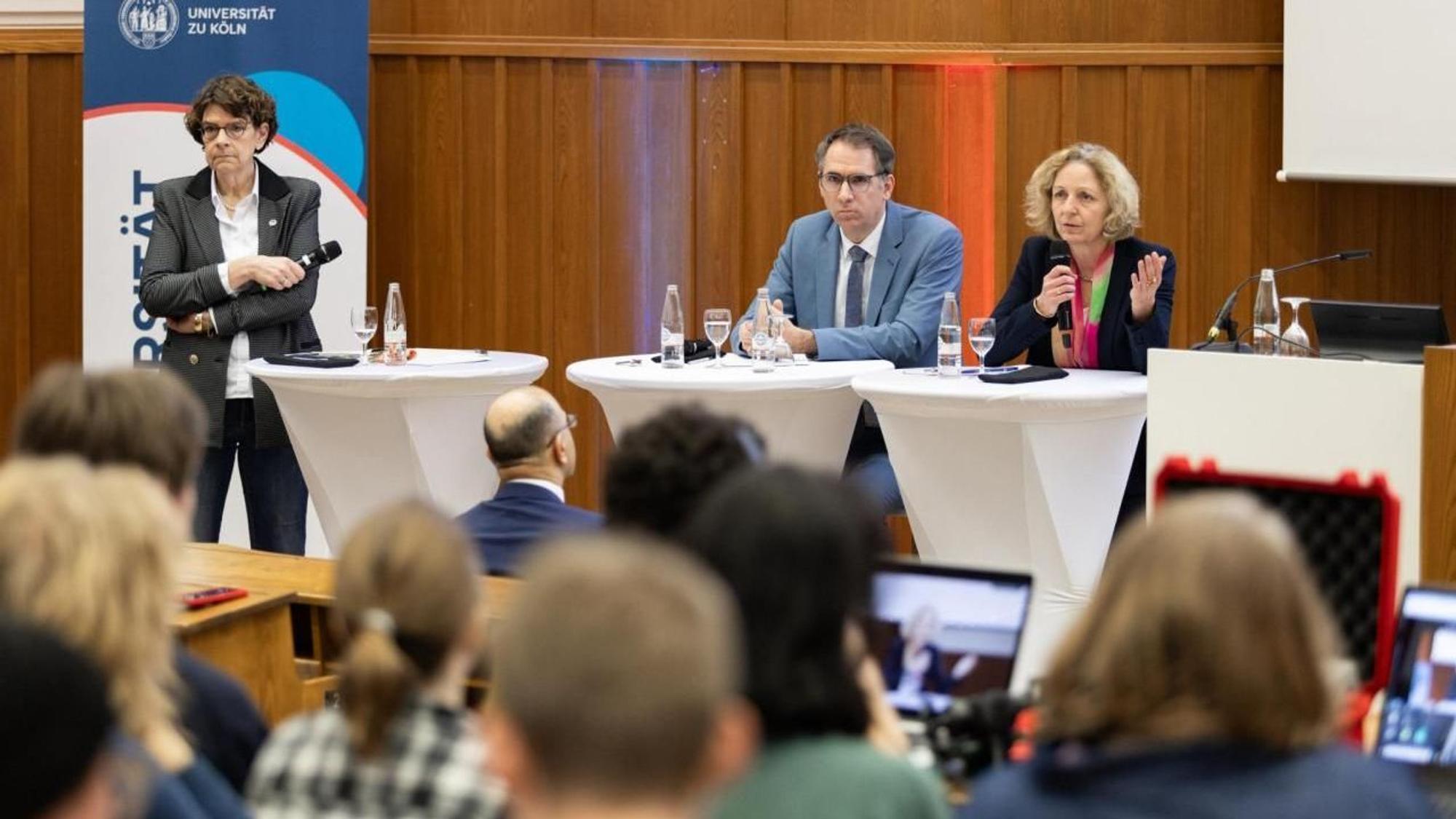 Hörsaal II der Uni Köln ist mit Studierenden und Mitarbeitenden dr Uni Köln gefüllt, vorne sitzen die Vortragenden.