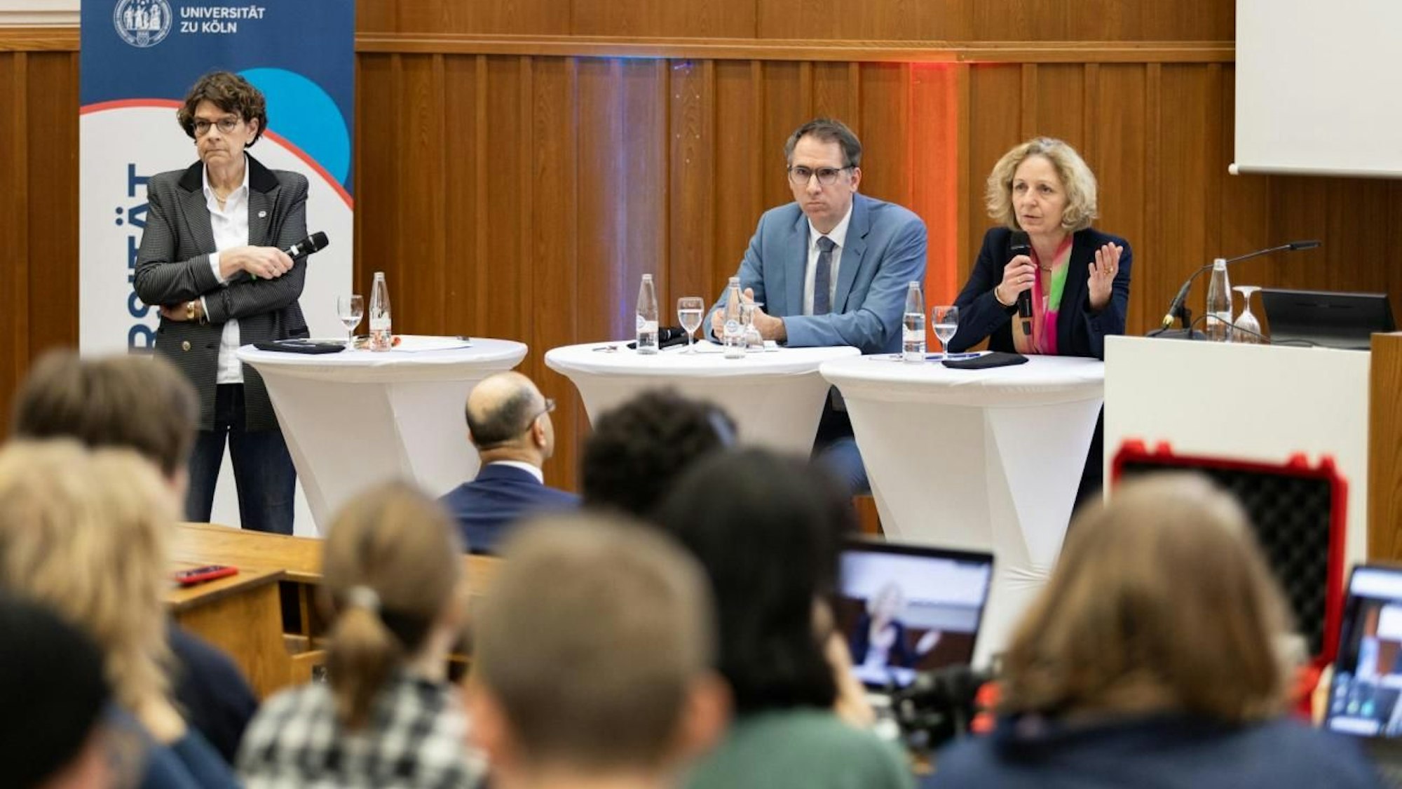 Hörsaal II der Uni Köln ist mit Studierenden und Mitarbeitenden dr Uni Köln gefüllt, vorne sitzen die Vortragenden.