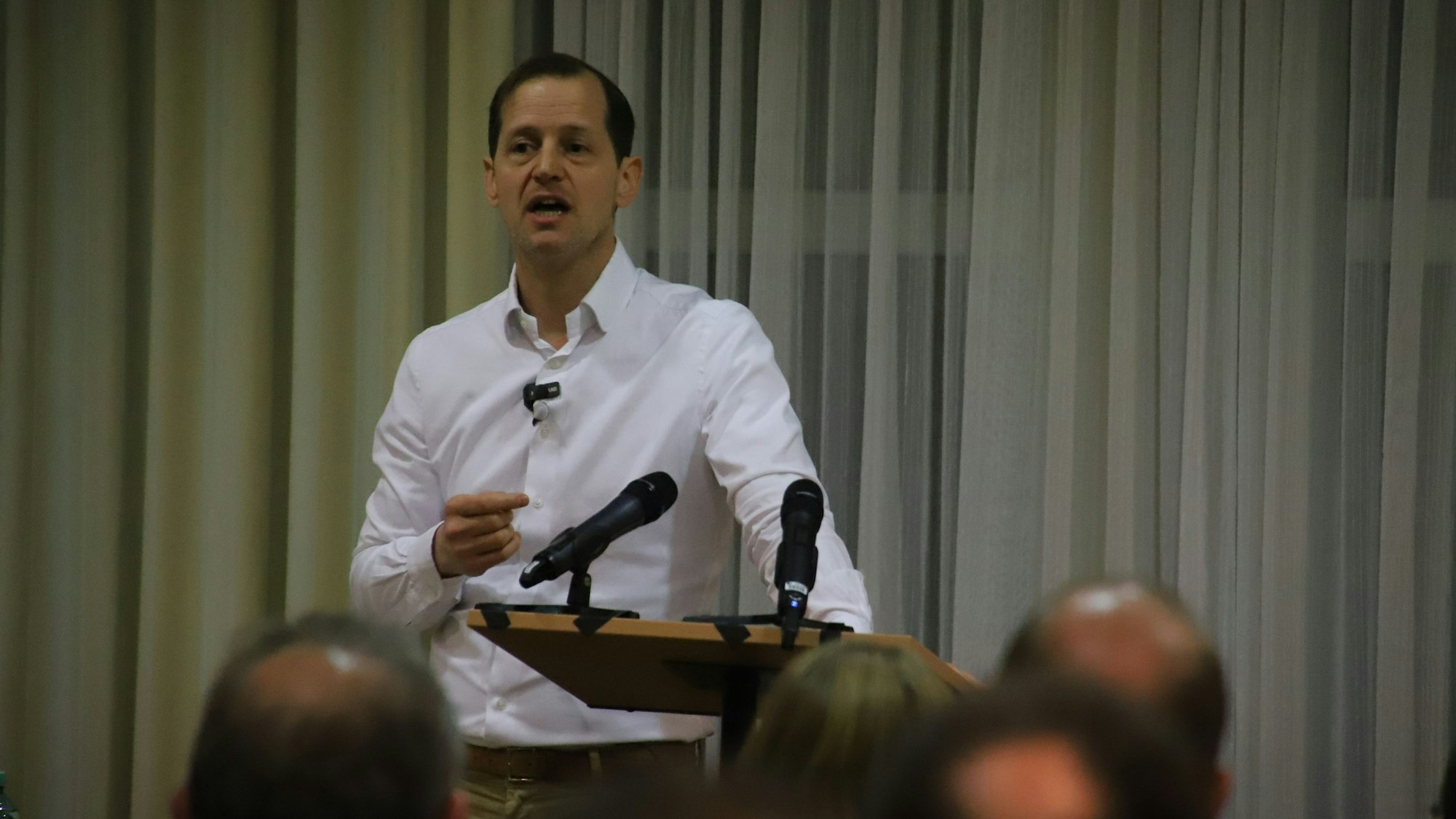 Ein Mann im weißen Hemd und Seitenscheitel steht an einem Rednerpult.