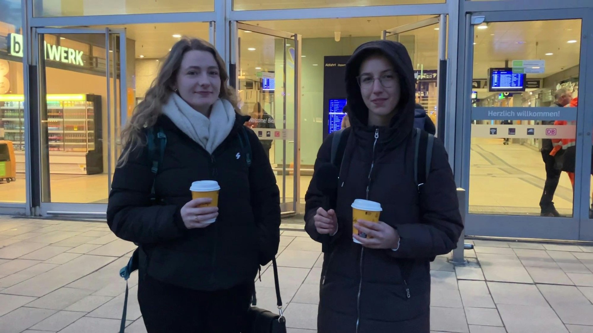 Zwei junge Frauen stehen mit Kaffeebechern in den Händen vor dem Kölner Hauptbahnhof.