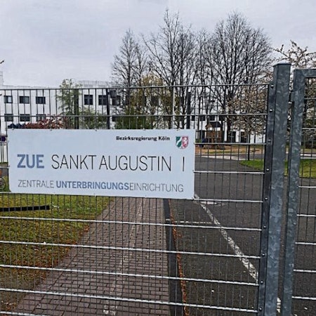 Ein Schild an einem Zaun weist auf die Zentrale Unterbringungseinrichtung für Geflüchtete (ZUE) in Sankt Augustin hin.