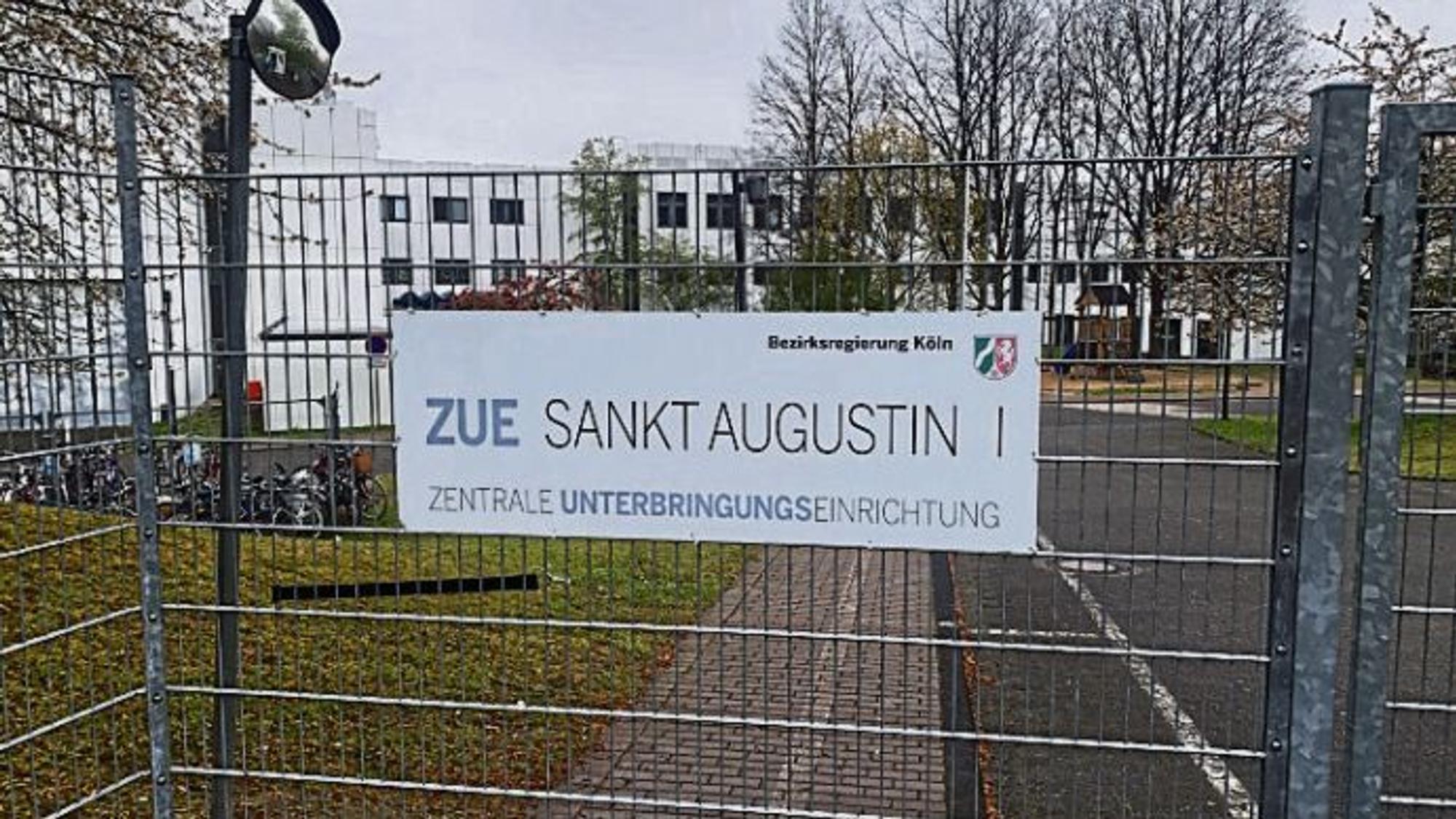 Ein Metallzaun mit einem Schild, auf dem ZUE Sankt Augustin steht.