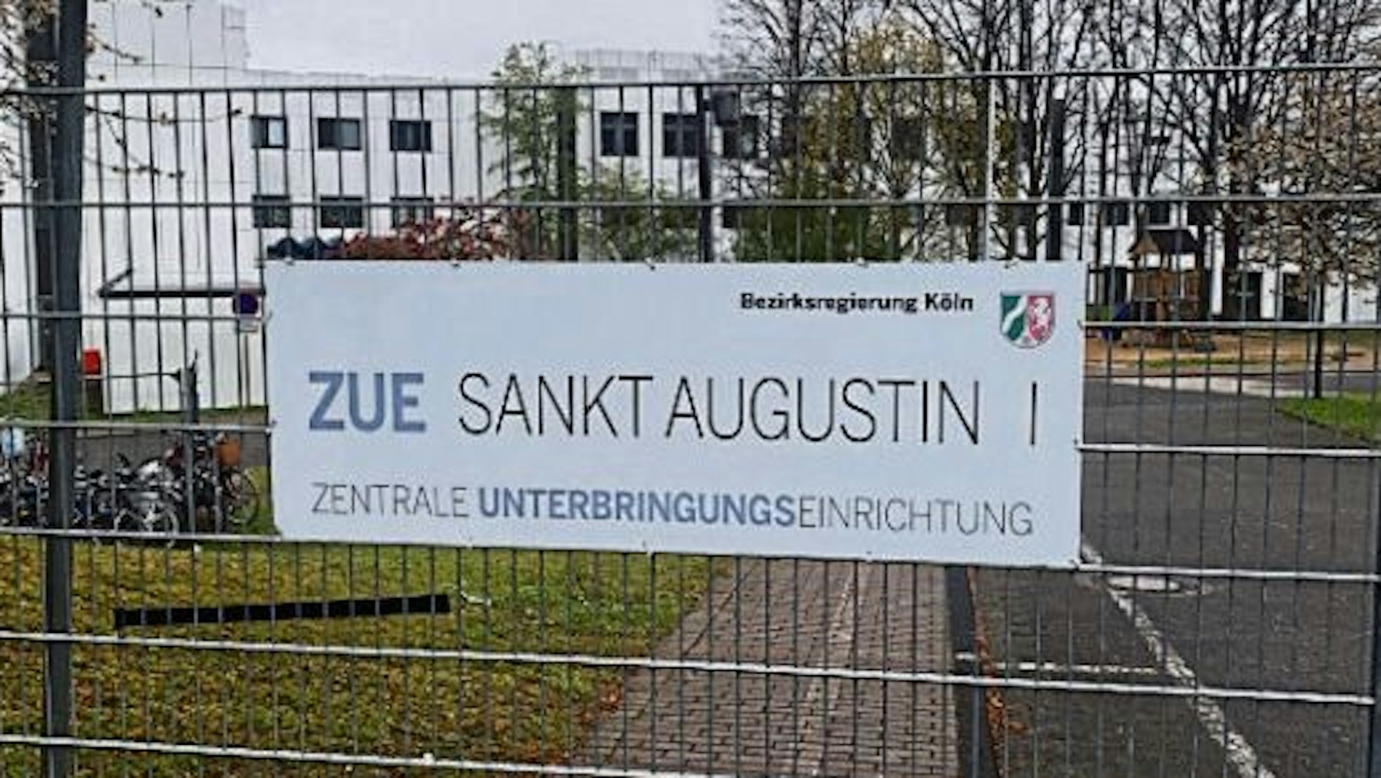 Am Zaun eines Grundstücks an der Heerstraße in Sankt Augustin weist ein Schild auf die Zentrale Unterbringungseinrichtung des Landes für Geflüchtete hin.