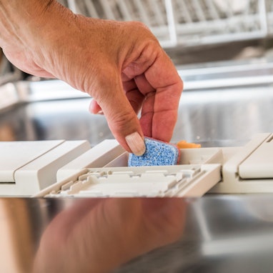 Eine Person befüllt eine Geschirrsplämaschine mit einem Geschirrspültab.