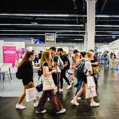 Jugendliche laufen mit Taschen durch eine Messehalle.