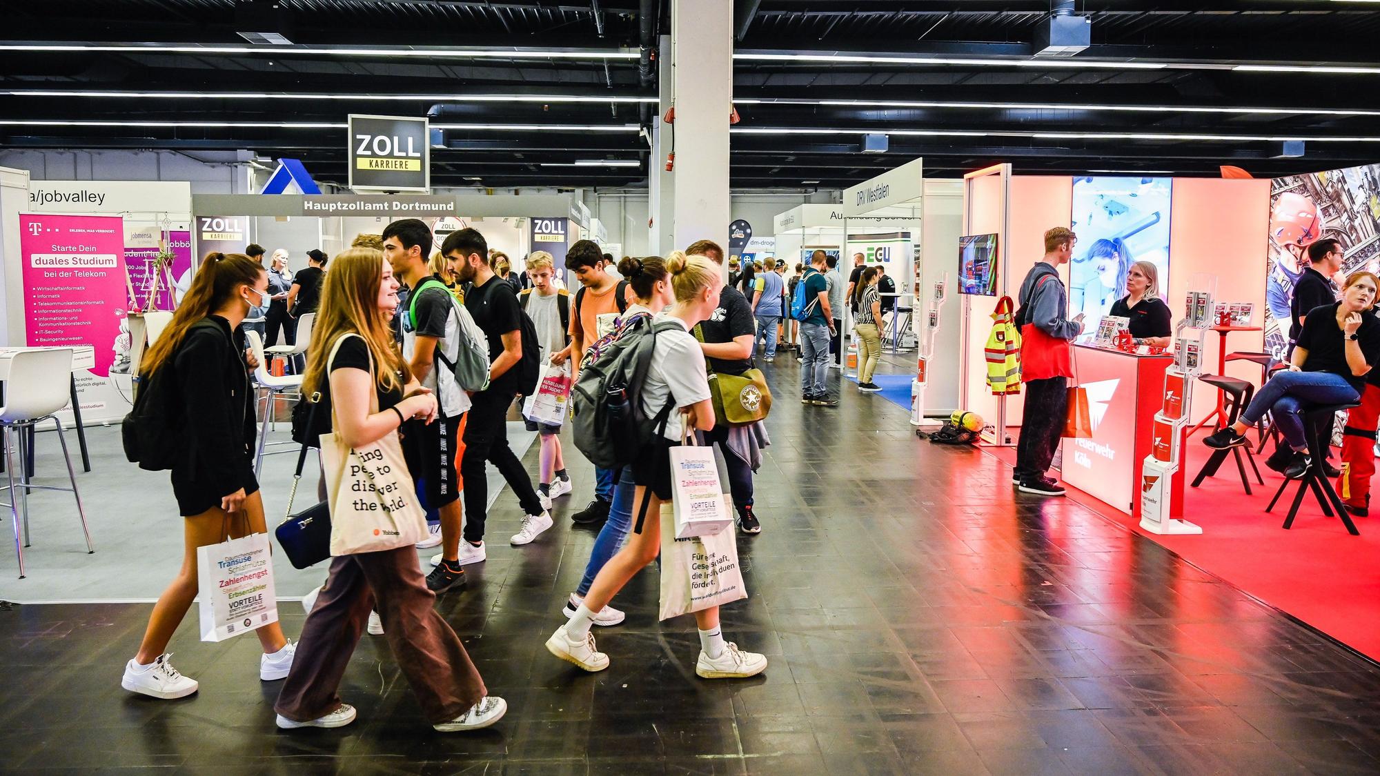 Jugendliche laufen mit Taschen durch eine Messehalle.
