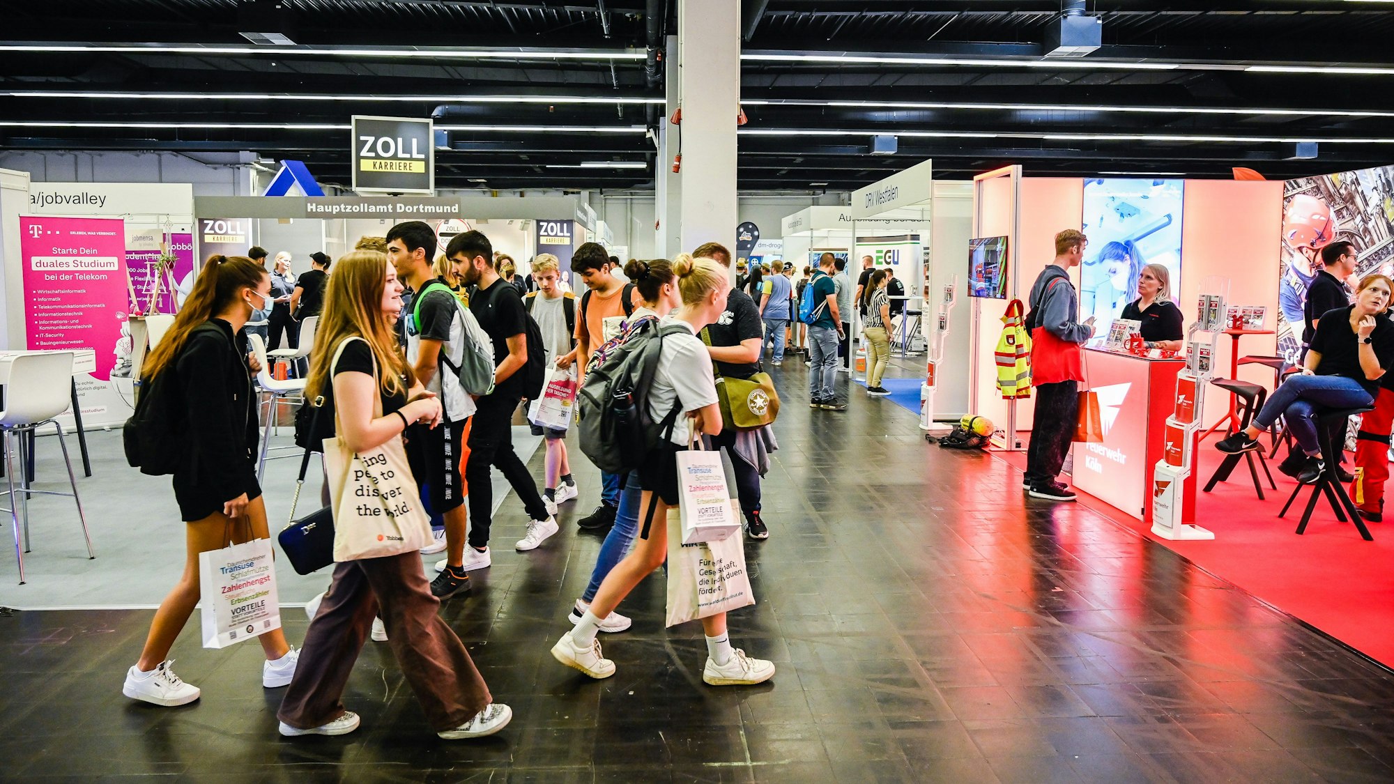 Jugendliche laufen mit Taschen durch eine Messehalle.