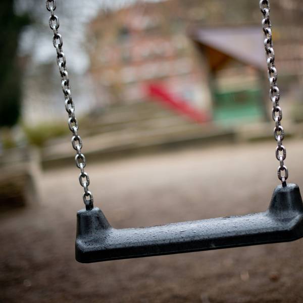 Auf dem Foto ist ein Spielplatz mit einer Schaukel im Vordergrund zu sehen.