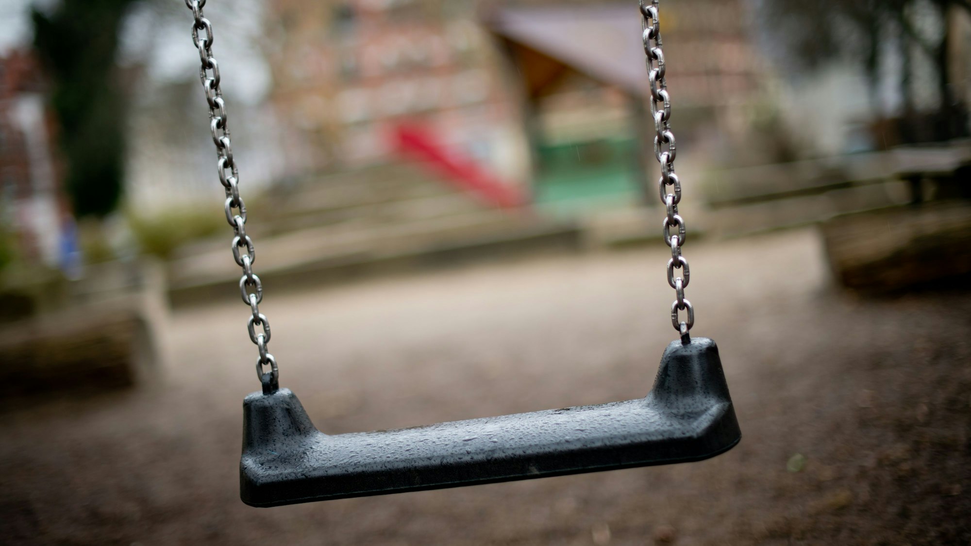 Auf dem Foto ist ein Spielplatz mit einer Schaukel im Vordergrund zu sehen.