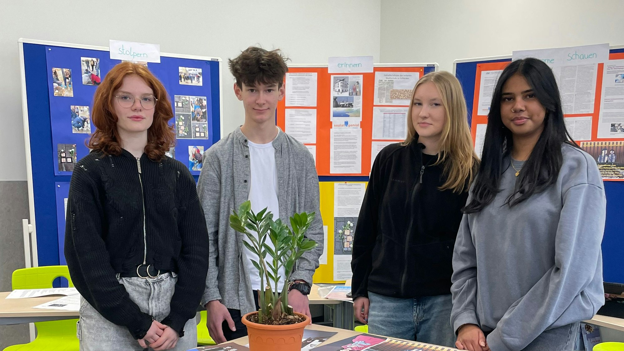 Drei Mädchen und ein Junge stehen in einem Klassenraum.