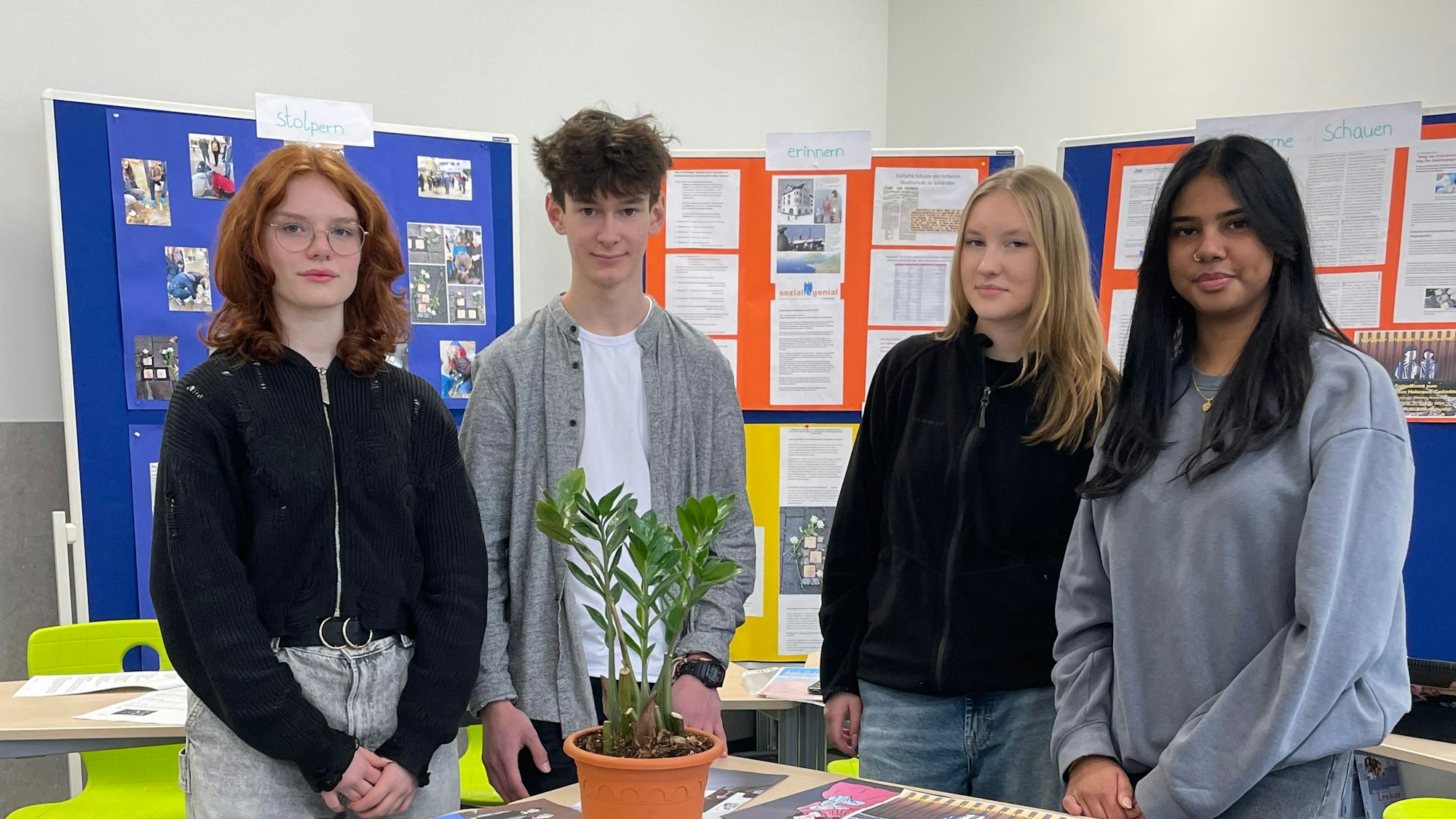 Drei Mädchen und ein Junge stehen in einem Klassenraum.