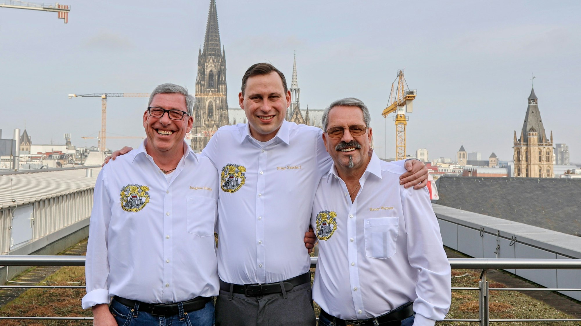 Das Dreigestirn in weißen Hemden auf einem Dach, im Hintergrund der Dom