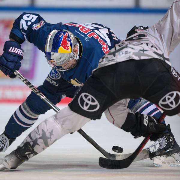 Eishockeyspieler fahren aus gegenübersetzten Richtungen auf einen Puck zu, bei dem sich ihre Schläger treffen.